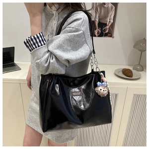 Detail of black glossy tote bag with silver chain and cute plush keychain accessory