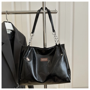 Detail of black patent leather tote bag with silver chain strap and leather logo tag