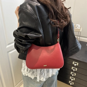 Sac sous le bras chic en cuir rouge avec logo doré porté par un mannequin stylé