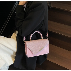 Sac rose brillant avec poignée tressée et bordure dorée porté par un modèle