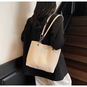 Detail of beige tote bag showing vertical stitching and metal chain shoulder straps