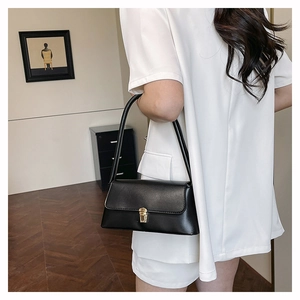 Detail of minimalist black baguette bag with gold square buckle shown on shoulder