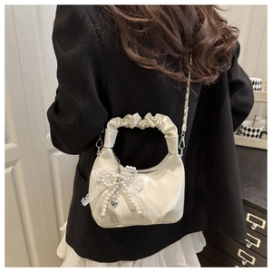 Close-up of cream pleated shoulder bag with lace bow, pearls, and heart charm detail