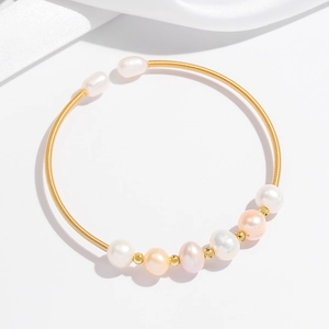 Detail eines goldenen Spiralarmreifs mit weißen und rosa Perlen auf seidigem Hintergrund