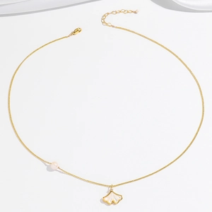 Detail van een gouden ginkgoblad ketting met schelpinleg en een elegante roze parel