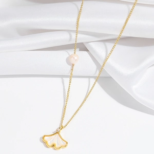 Detail van gouden ginkgoblad ketting met parelmoer inleg en een elegante witte parel