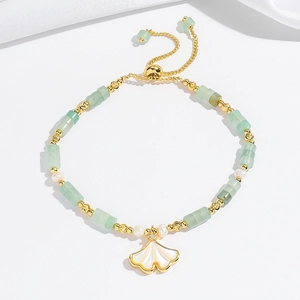 Detailopname van ginkgoblad armband met groene stenen en parels op witte zijde
