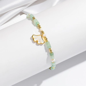 Detailopname van de ginkgoblad-armband met groene kralen en gouden accenten