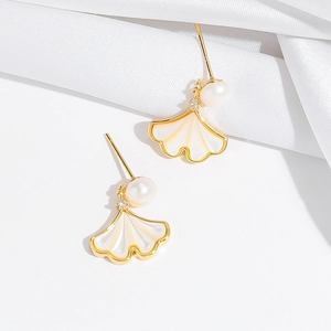 Gouden ginkgo oorbellen met witte schelpinleg en parel op een witte zijden achtergrond