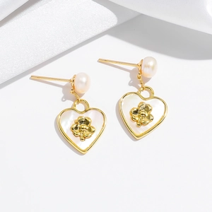 Close-up of heart-shaped pearl earrings with gold four-leaf clover motif and silk detail