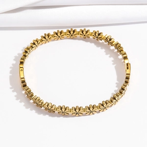 Detailed view of a gold stainless steel daisy floral bangle on white silk background