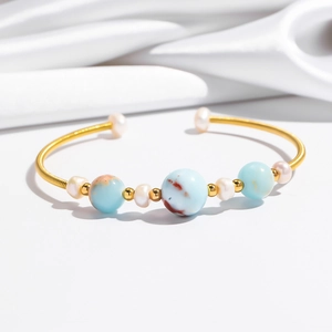 Detail of gold spiral cuff bracelet featuring blue stone beads and white pearls
