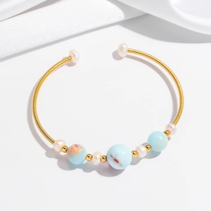 Detail view of a gold spiral bangle with light blue stones and white pearls on white silk