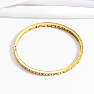 Detail of gold stainless steel bangle featuring classic Greek meander pattern engraving