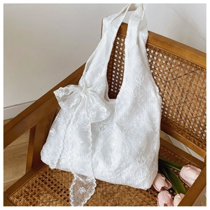 Close-up of a white lace tote bag with floral embroidery and bow on a vintage chair