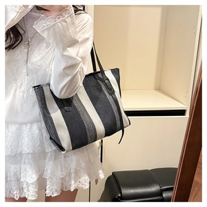 Detailed view of a large canvas tote bag with vertical stripes and black leather straps