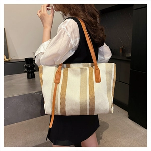 Detail of striped canvas tote bag with brown leather handles in a modern lifestyle setting