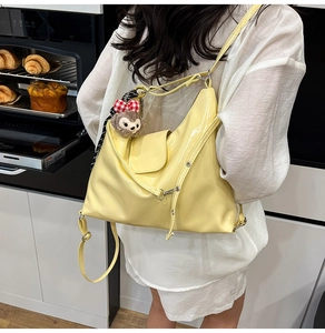 Detail of glossy yellow patent leather tote bag featuring a plush cartoon bear charm