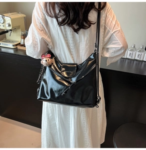 Detail of black glossy hobo bag with teddy bear pendant and branded lettering logo