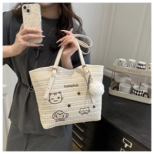 Détail du sac cabas en paille tressée avec broderie chat et pompon blanc décoratif