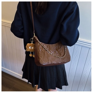 Detail of dark brown pleated leather tote bag with gold chain and plush cookie charm