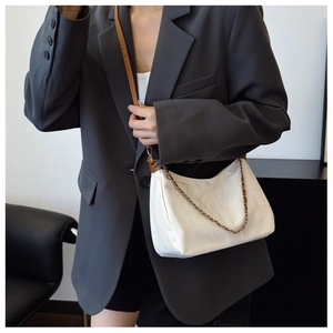 Detail of minimalist cream tote bag with metal chain and brown leather shoulder strap