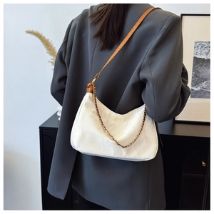 Detail of white crescent bag with embossed texture and gold chain strap on grey blazer