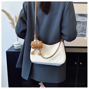 Close-up of textured white tote bag with gold chain and plush monster charm detail