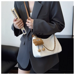 Detail of white crescent tote bag with brown plush pendant and metal chain strap