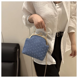 Detail of blue denim jacquard handbag with gold metal frame and chain strap on model