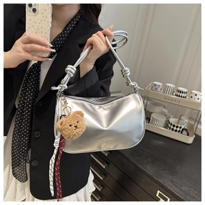 Silver metallic crossbody bag featuring a knotted handle and cute plush bear charm detail