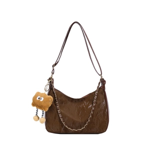 Brown textured hobo bag with gold chain and cute plush monster charm on white background