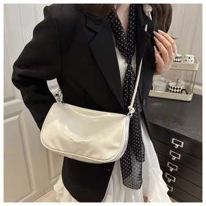 Gros plan d'un sac demi-lune en cuir verni crème porté par un mannequin en tenue décontractée