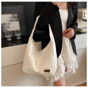 Close-up of a white soft PU tote bag featuring a minimalist brown leather brand tag detail