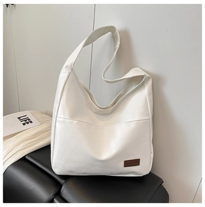 Detail of soft white PU leather tote bag with brown brand tag on a black leather background