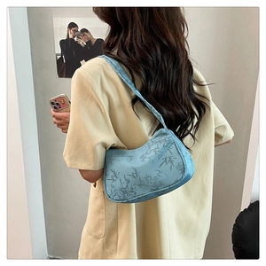 Blue crescent shoulder bag with bamboo leaf print worn by a model on a beige shirt