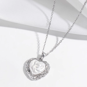 Détail du collier cœur argenté avec bord tissé et motif floral blanc au centre du bijou