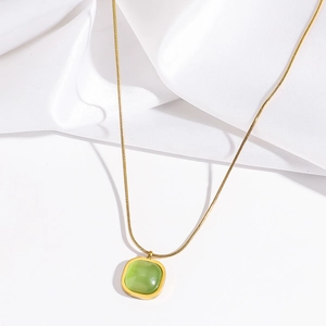 Detail view of a gold titanium square necklace with green resin pendant on white silk