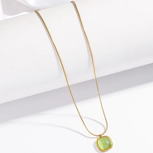 Close-up of a gold snake chain necklace with a square green gemstone on white silk