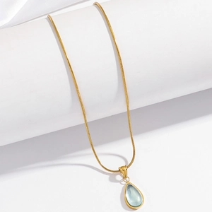 Detailed view of a gold snake chain necklace featuring a blue teardrop pendant
