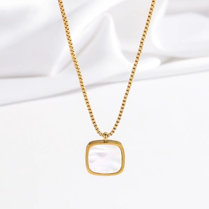 Détail du collier carré doré avec pendentif en nacre blanche sur tissu de soie
