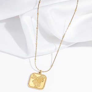 Detail of a gold square rose relief pendant on a delicate bead chain over silk