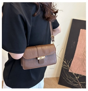 Detail of crocodile pattern leather and bamboo-shaped gold buckle on a brown shoulder bag