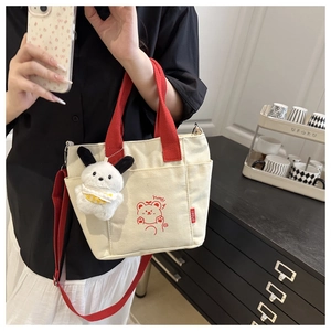 Detail of canvas tote bag with red handles, cartoon bear print and plush puppy charm
