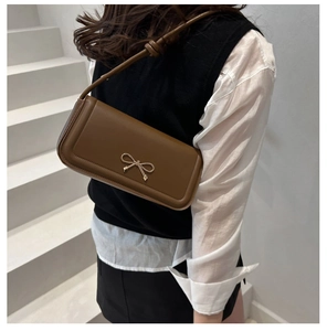 Détail d'un sac baguette en cuir marron avec boucle nœud dorée porté par un modèle