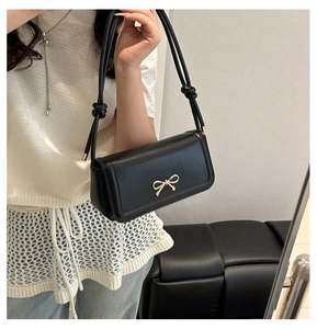 Détail d'un sac à bandoulière en cuir noir avec une boucle dorée en forme de nœud chic