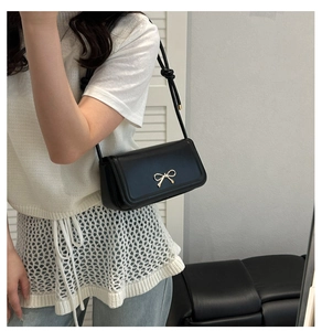 Détail du sac bandoulière en cuir noir avec nœud doré et bandoulière à nœuds chic