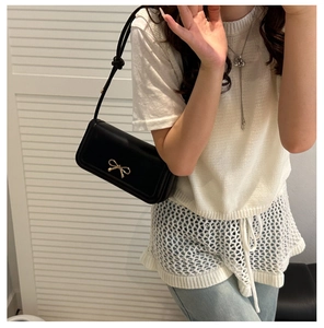 Détail du sac sous le bras rectangulaire noir avec nœud en métal doré et texture en cuir