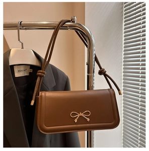 Détail du sac baguette en cuir marron caramel avec nœud doré et bandoulière nouée