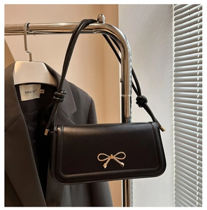Détail d'un sac à main noir en cuir brillant avec boucle nœud dorée et bandoulière nouée